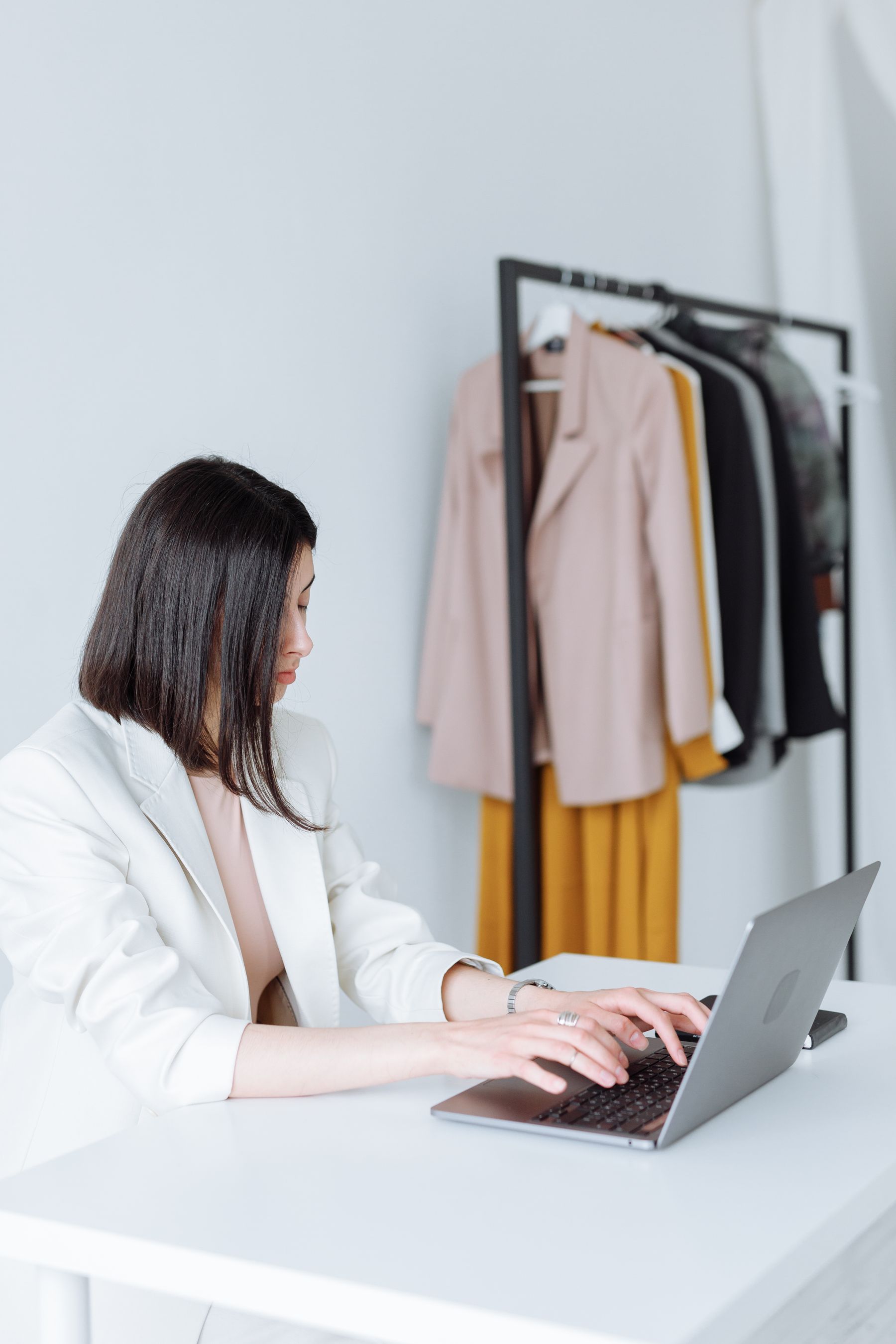 Vrouw werkt op een laptop naast een kledingrek