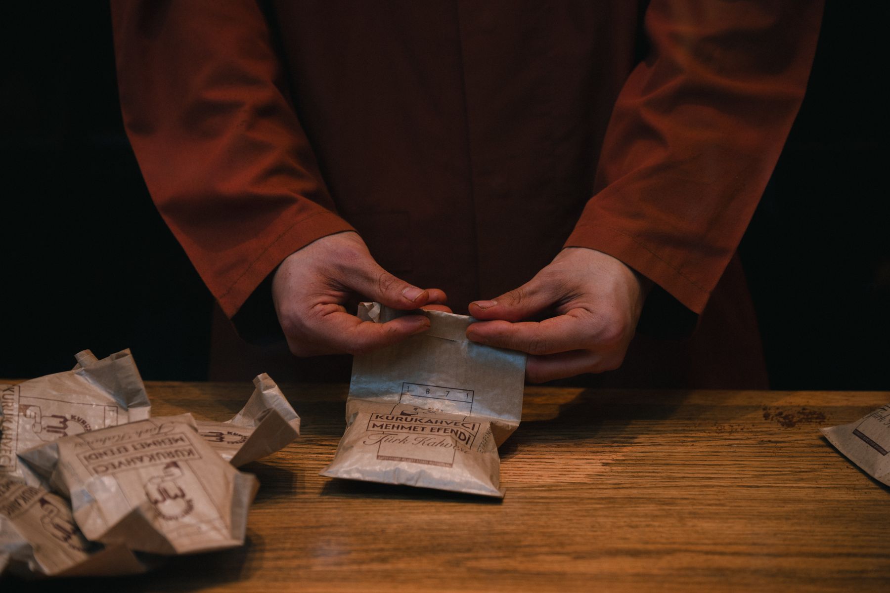Een medewerker sluit papieren koffiezakken aan een houten werktafel